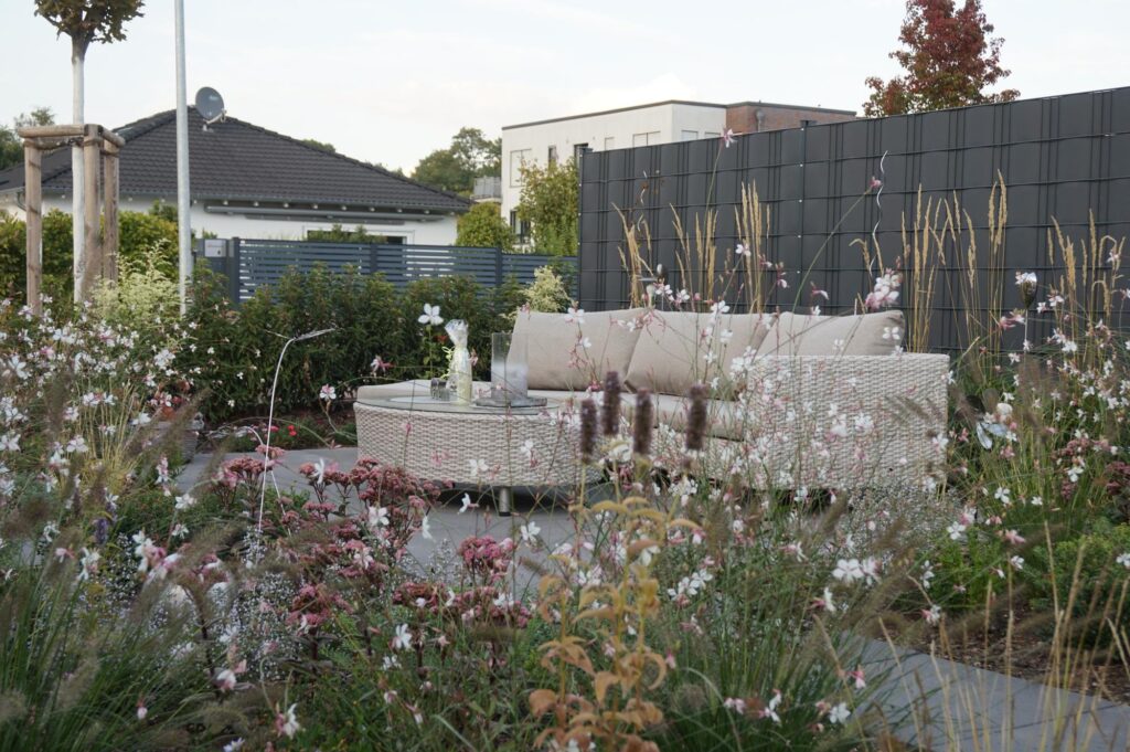 Moderne Terrasse mit beigem Loungesofa, umgeben von blühenden Wildblumen und Ziergräsern - ein inspirierendes Beispiel für professionelle Gartenplanung und individuelle Pflanzplanung im Garten. Ideal für die Gartenneugestaltung im Münsterland.