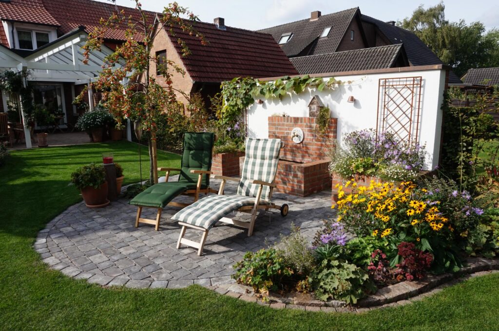 Ein gemütliches Gartenpatio mit zwei Lounge-Stühlen, umgeben von blühenden Pflanzen und einer harmonischen Bepflanzung, lädt zum Entspannen ein. Das Ambiente eignet sich ideal als Inspiration für eine professionelle Gartenplanung im Münsterland oder Kreis Borken.